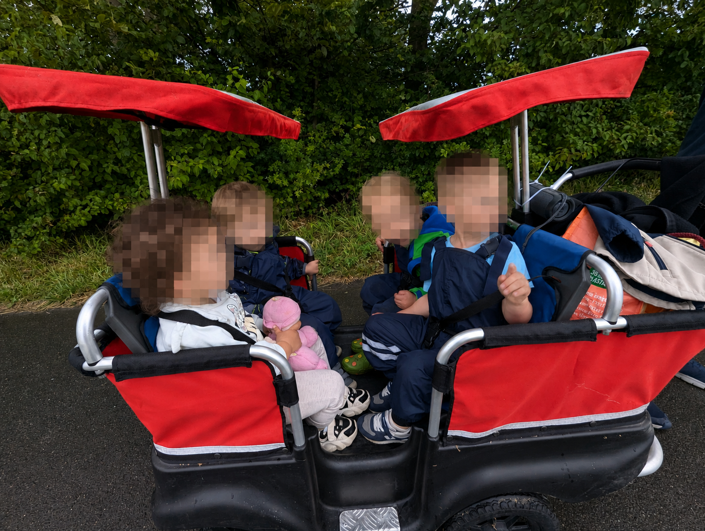 Kinder sitzen angeschnallt im roten Turtlebus bei einem Spaziergang im Grünen